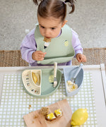 A child using the Lassig Cutlery with Silicone Handle  featuring Happy Fruits Lemon design. This children's cutlery set is part of a wide range of tableware available at Babipur.
