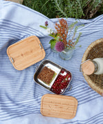 The Lassig Stainless Steel Bamboo Lunchbox with a Garden Explorer design shown open and filled with food. This stainless steel lunchbox is part of a wide range of reusable food containers available at Babipur. 