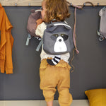 A child wearing the Lassig tiny kids backpack in grey, with a racoon face printed on and 3D ears and tail.