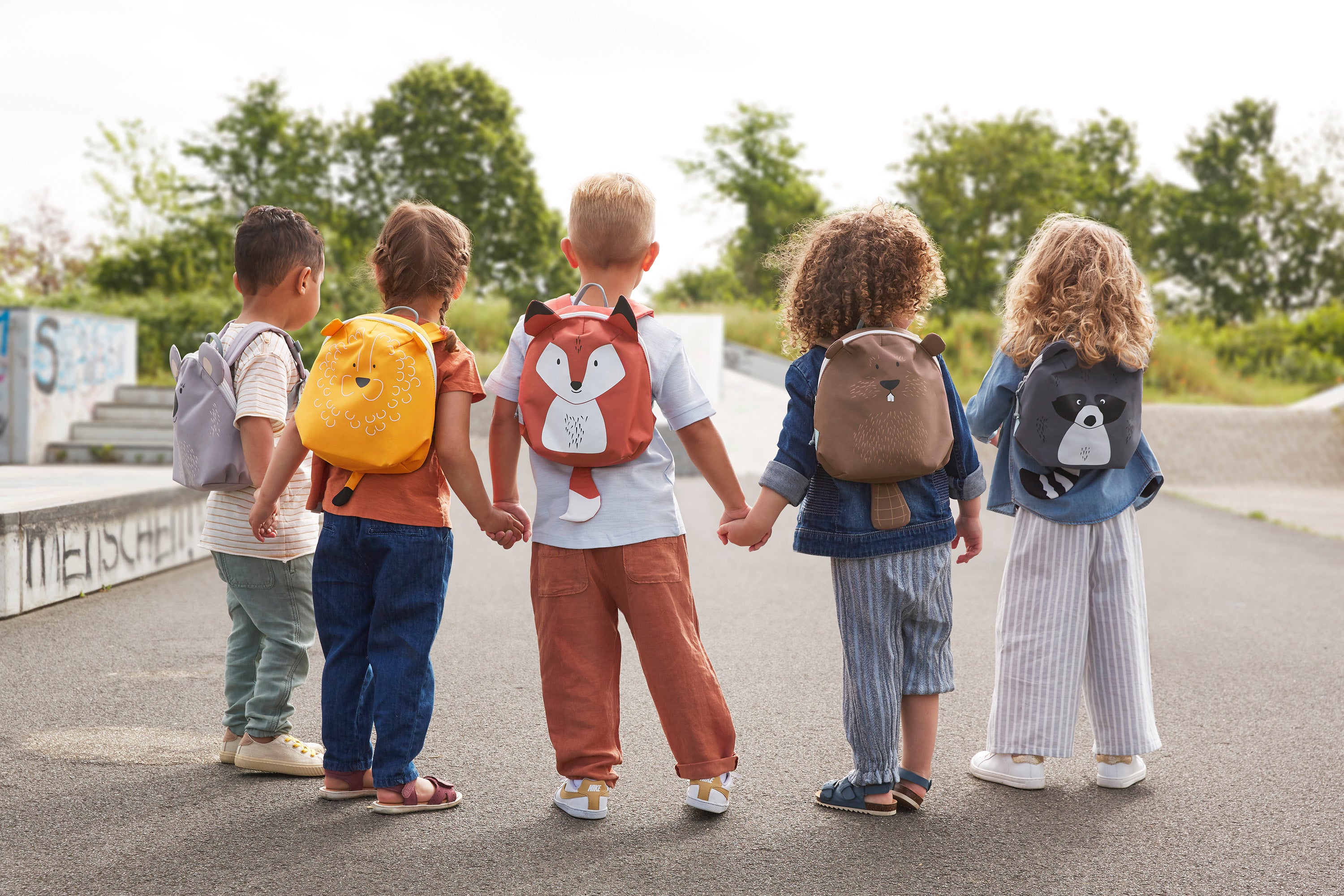 A group of children holding hands, all wearing different 'About Friends' tiny backpacks from Lassig with different animals. 