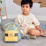 A child sitting on a carpet floor in a playroom next to the Lassig kids tiny digger backpack 