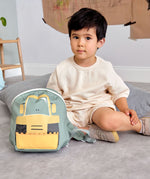 A child sitting on a carpet floor in a playroom next to the Lassig kids tiny digger backpack 