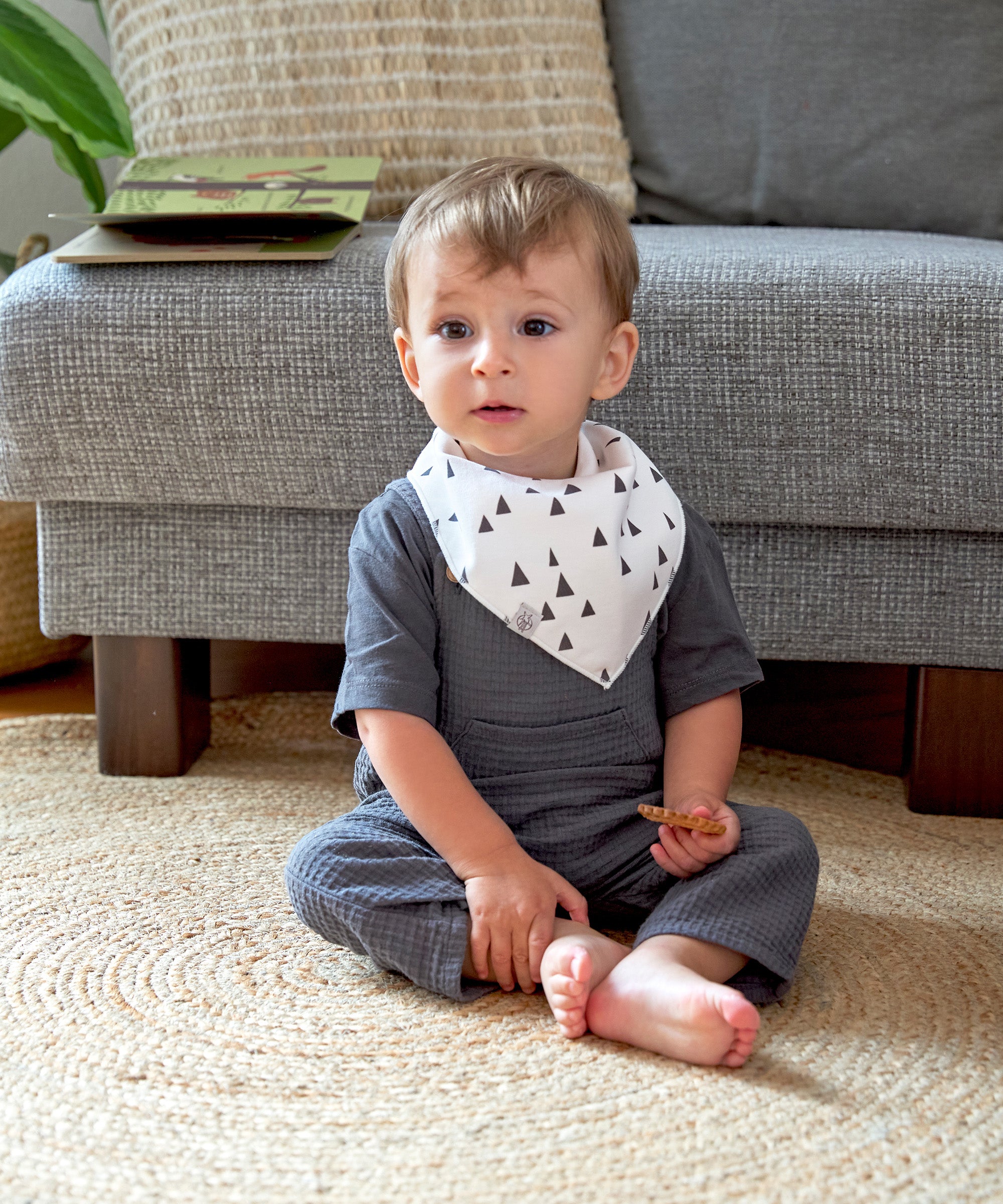 A baby wearing the Lassig organic cotton bandana bib, in white with grey triangles.