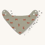 Two Lassig organic cotton bandana bibs, one in green with little foxes printed all over, and one in white with grey triangles.