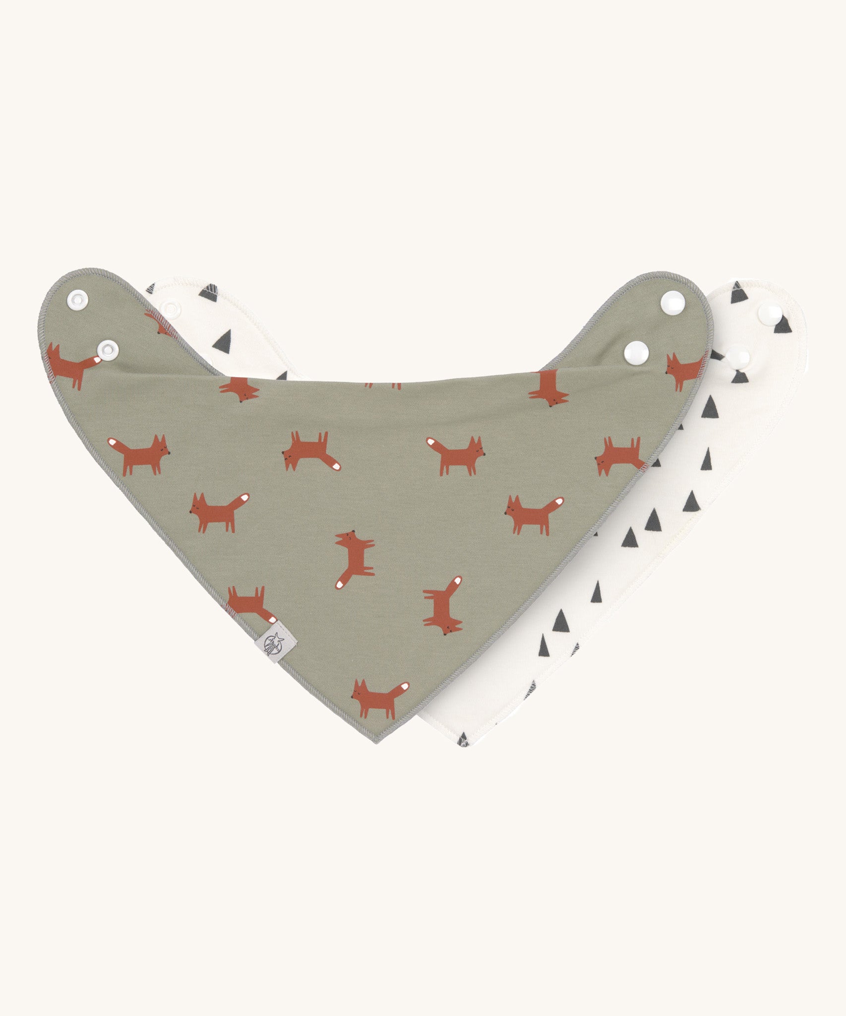 Two Lassig organic cotton bandana bibs, one in green with little foxes printed all over, and one in white with grey triangles.