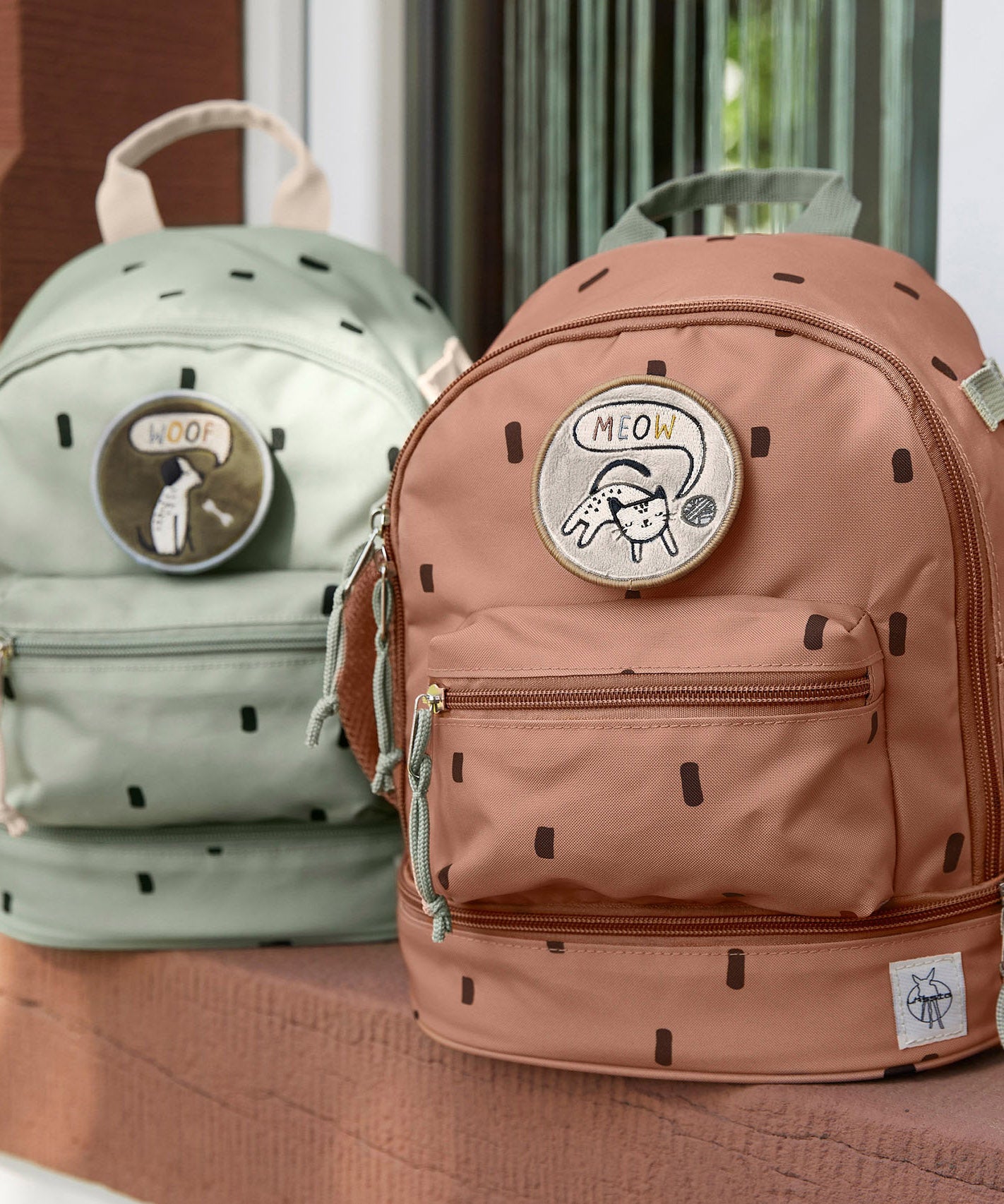 Lassig kids mini party caramel and olive pattern backpacks outside on a step. Features padded shoulder straps, mesh side pockets, a handy loop handle on the top and 3 zipped compartments. 
