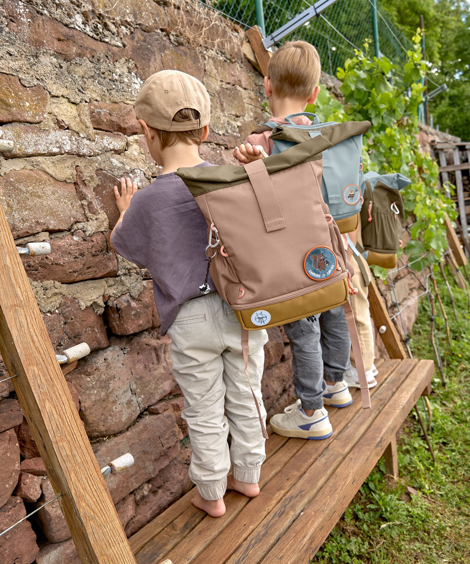 A child wearing the Lassig Mini Rolltop Backpack in a Nature Hazelnut colour. This children's bag is part of a wide range of backpacks and accessories available at Babipur. 