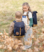 Two children wearing Lassig mini backpacks in navy blue, in a green field. 