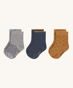 The Lassig 3 pack of organic cotton baby socks, one pair is grey with blue stripes, one is navy with mustard yellow trim on the cuffs, and one is mustard yellow with navy dots.
