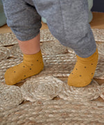 A baby's feet, wearing the Lassig organic cotton baby socks in mustard yellow with navy dots.