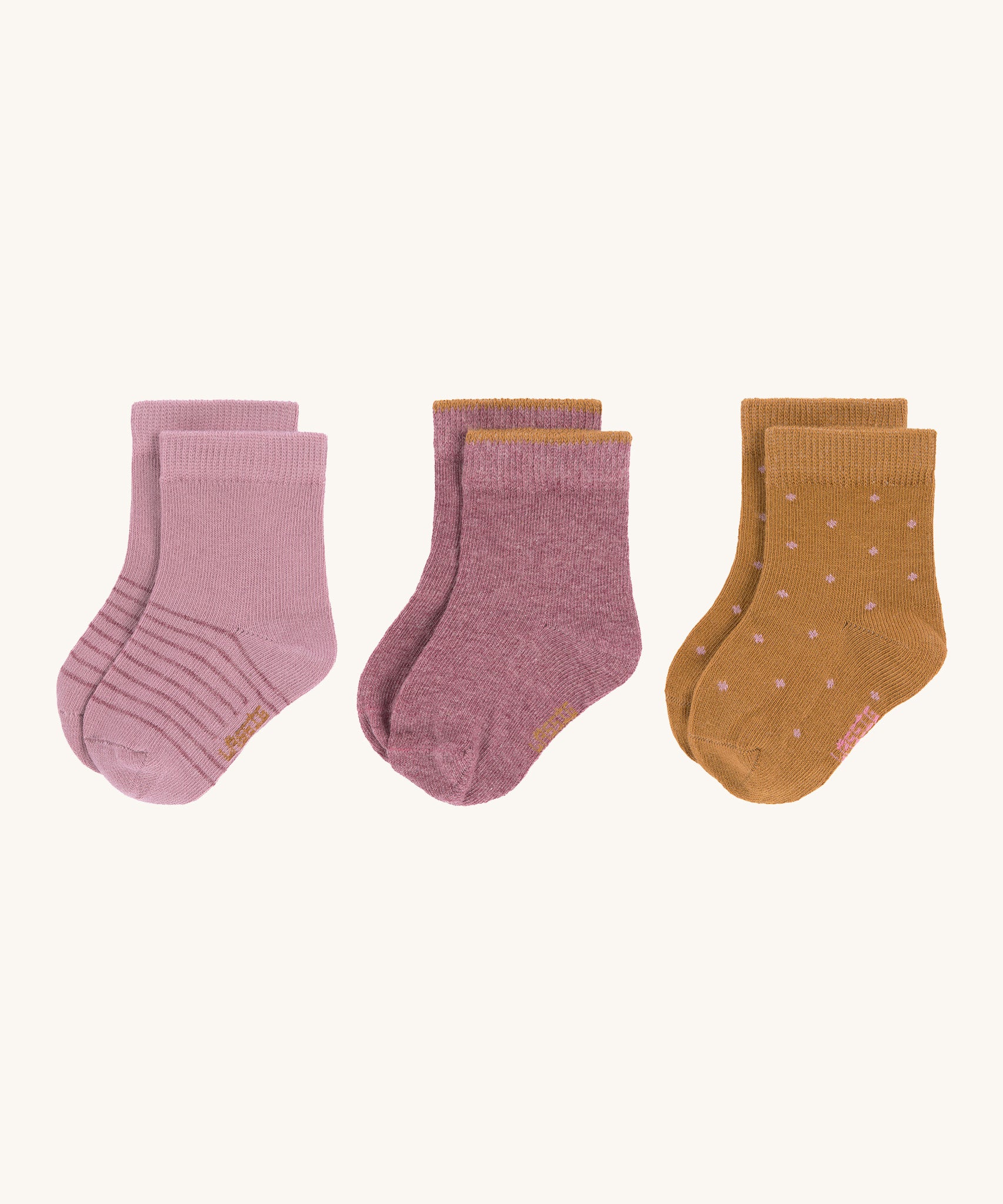 The Lassig 3-pack of organic cotton baby socks, one pair is light pink with darker pink stripes, another is in a darker pink with mustard yellow trims on the cuffs, and one is mustard yellow with light pink dots.