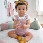 A baby sat down, wearing the Lassig organic cotton baby socks in mustard yellow with pink dots. 
