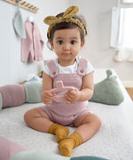 A baby sat down, wearing the Lassig organic cotton baby socks in mustard yellow with pink dots. 
