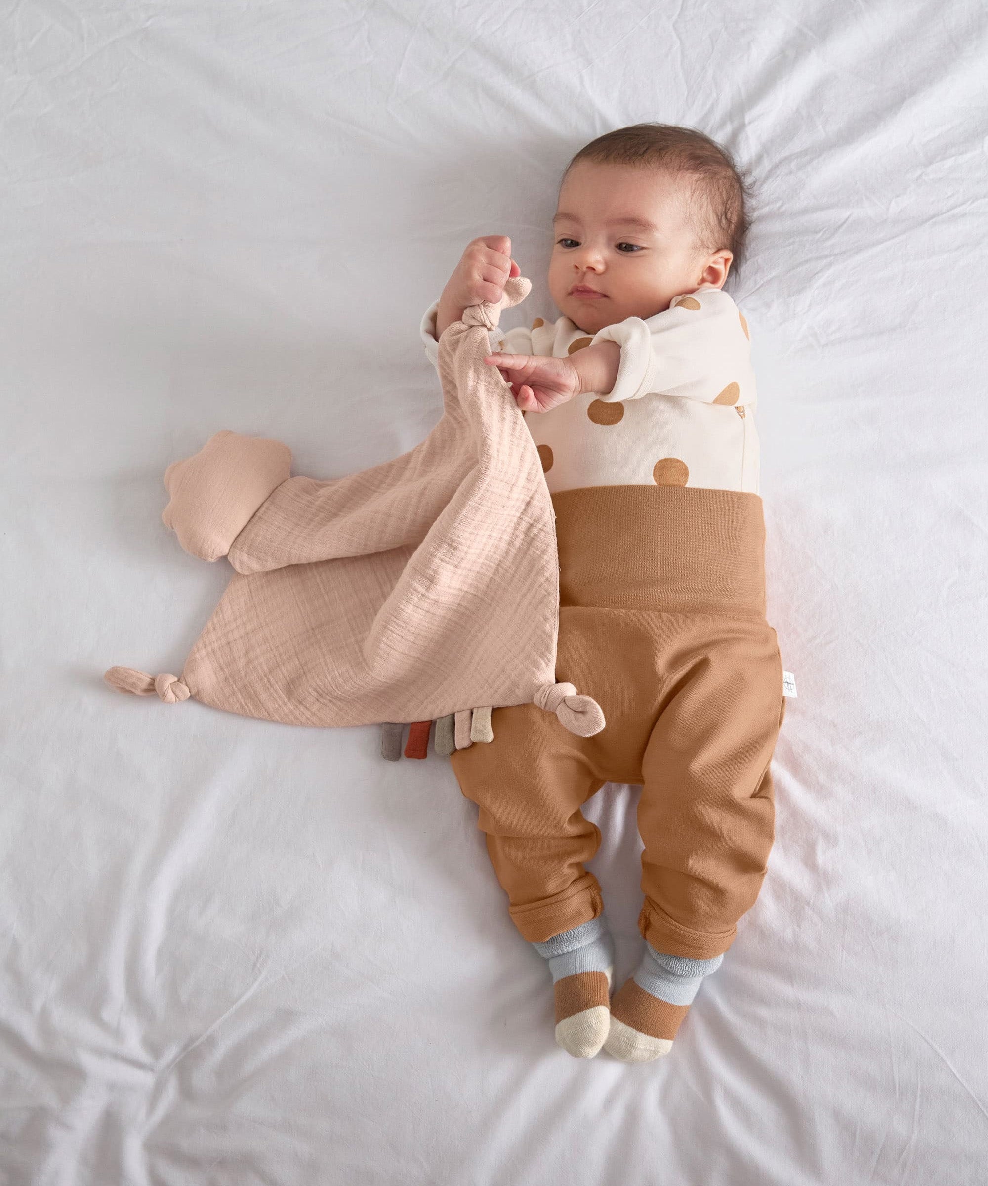 A baby playing with the Lassig organic cotton muslin comforter.