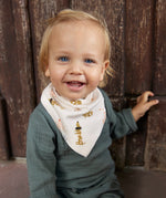 A smiling baby in a Lassig organic cotton muslin outfit in petrol green, and a Lassig dribble bib. 