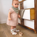 A baby wearing the Lassig organic cotton muslin dress with a bandana dribble bib.