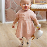 A little toddler wearing the Lassig organic cotton muslin dress in a pretty powder pink colour.