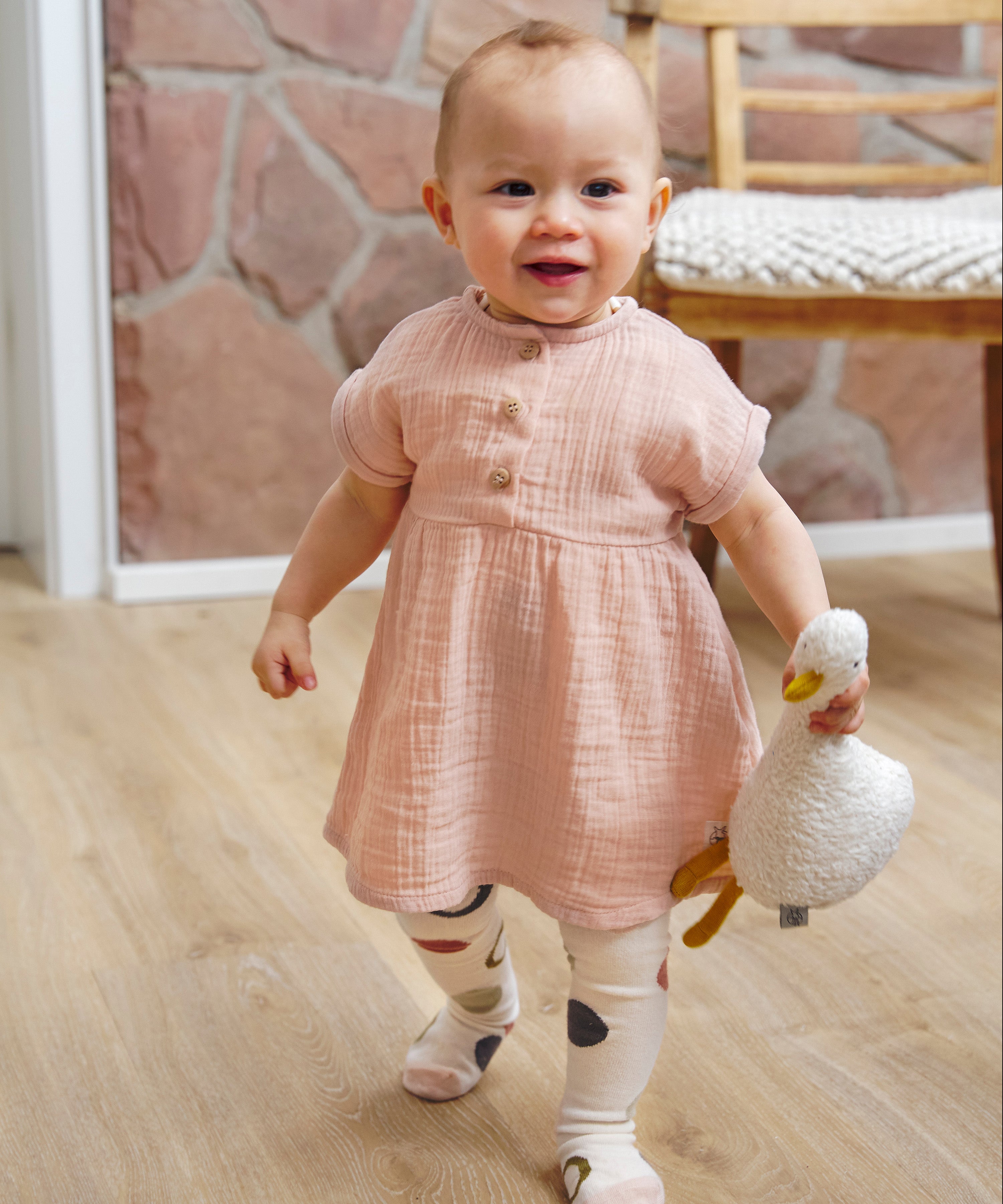A little toddler wearing the Lassig organic cotton muslin dress in a pretty powder pink colour.