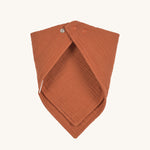 The Lassig organic cotton muslin bandana dribble bib in a lovely orange rust colour, with little metal push-in fastenings at the neck.