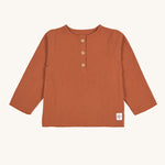 The Lassig organic cotton muslin shirt for babies and toddlers, in a bright orange rust colour with little brown buttons.