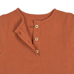 A closeup of the buttons on the Lassig organic cotton muslin shirt for babies and toddlers, in a bright orange rust colour.