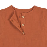 A closeup of the buttons on the Lassig organic cotton muslin shirt for babies and toddlers, in a bright orange rust colour.