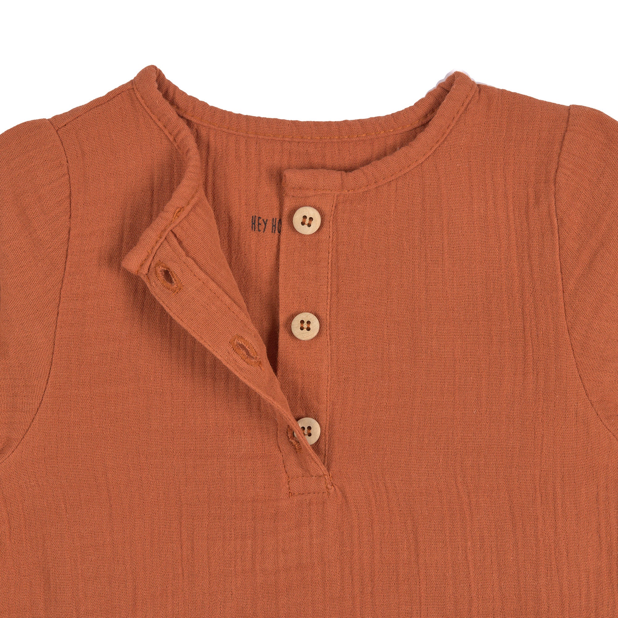 A closeup of the buttons on the Lassig organic cotton muslin shirt for babies and toddlers, in a bright orange rust colour.