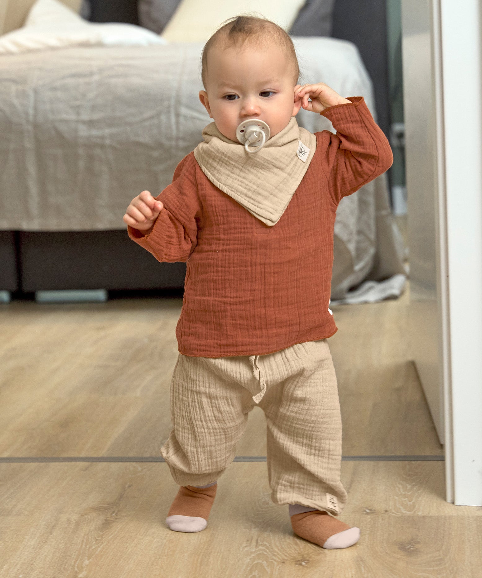 A little toddler wearing the Lassig organic cotton muslin shirt for babies and toddlers, in a bright orange rust colour.