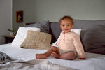 A baby sat on a bed, wearing the Lassig organic cotton muslin long sleeved top for babies and toddlers, in a beautiful pale powder pink colour.
