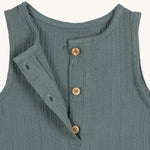A closeup of the brown buttons at the neck of the Lassig organic cotton muslin jumpsuit in petrol green. 