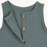 A closeup of the brown buttons at the neck of the Lassig organic cotton muslin jumpsuit in petrol green. 
