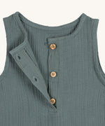 A closeup of the brown buttons at the neck of the Lassig organic cotton muslin jumpsuit in petrol green. 