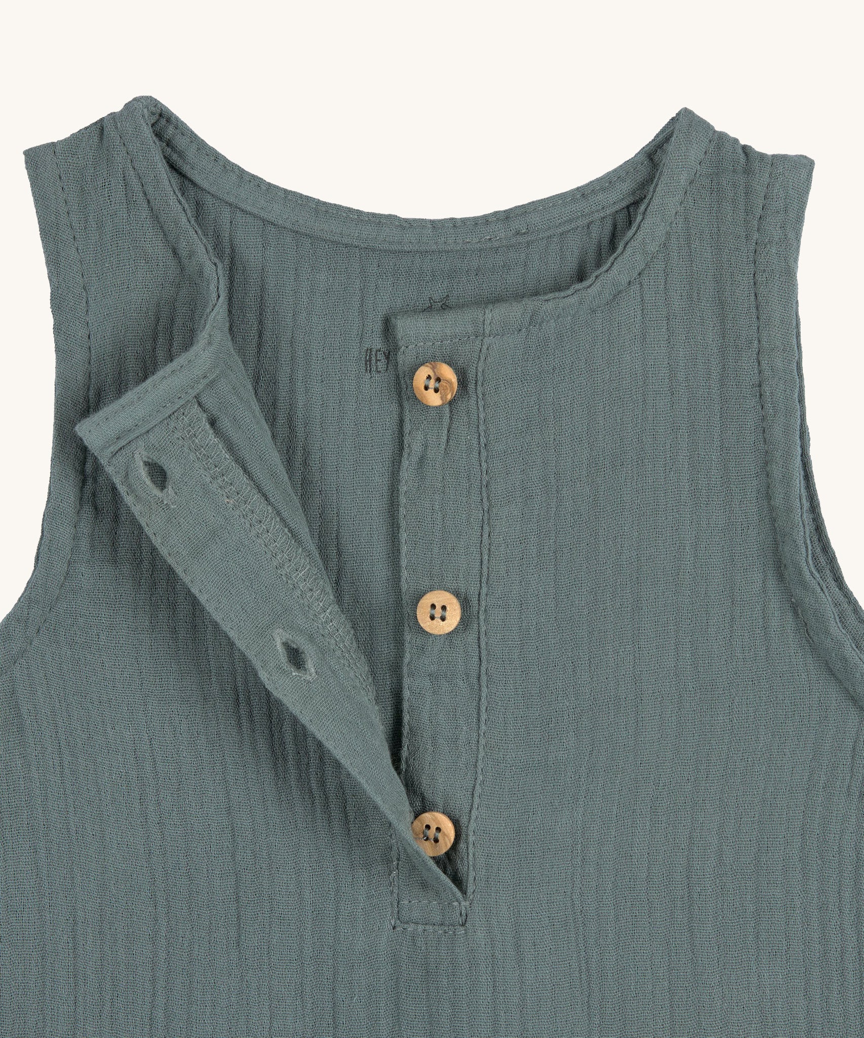 A closeup of the brown buttons at the neck of the Lassig organic cotton muslin jumpsuit in petrol green. 