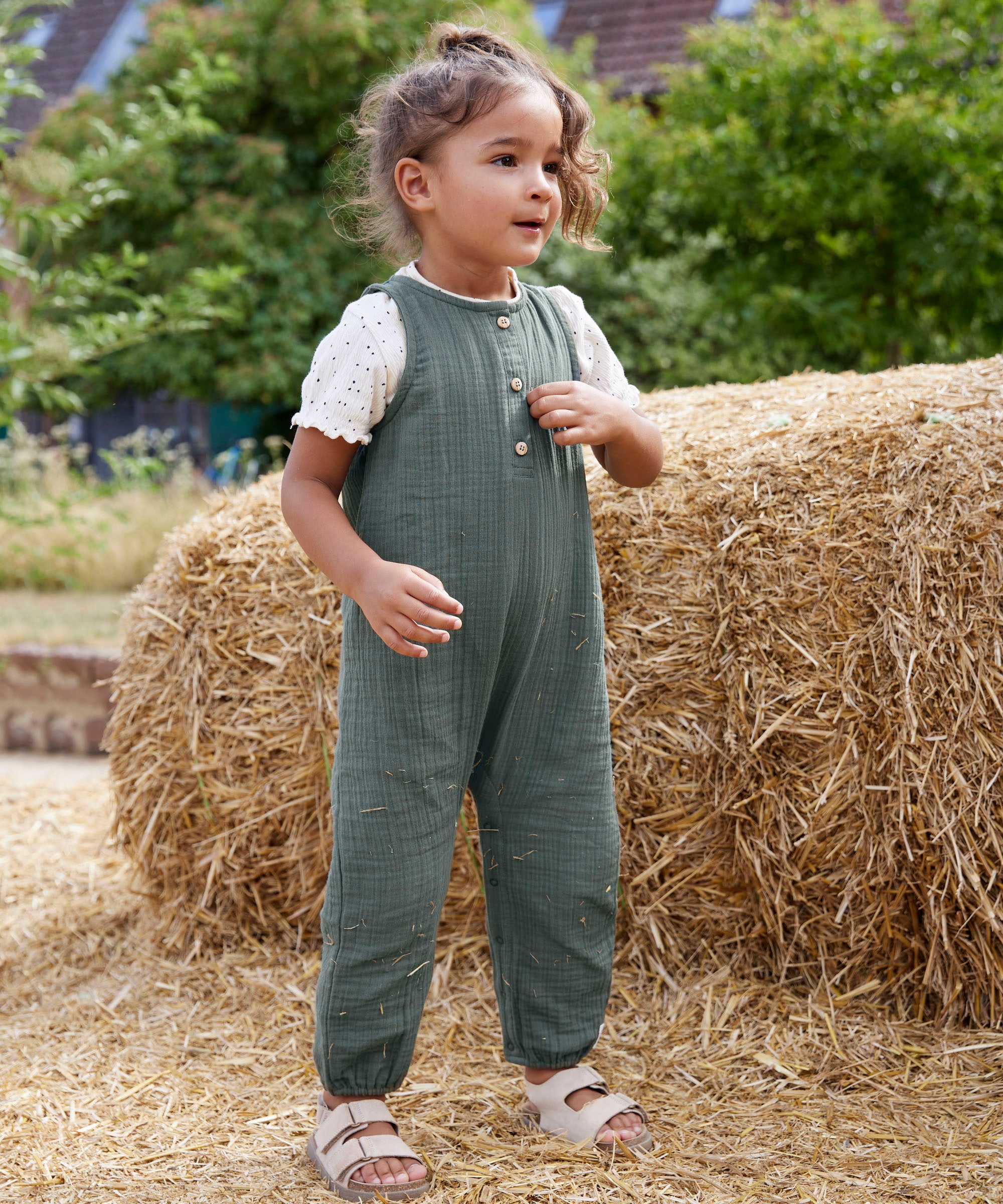 A child wearing the lassig organic cotton muslin jumpsuit in petrol green. 