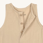 A closeup of the Lassig organic cotton muslin baby and toddler jumpsuit in a natural cream colour, showing the three cream buttons at the neck.