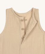 A closeup of the Lassig organic cotton muslin baby and toddler jumpsuit in a natural cream colour, showing the three cream buttons at the neck.