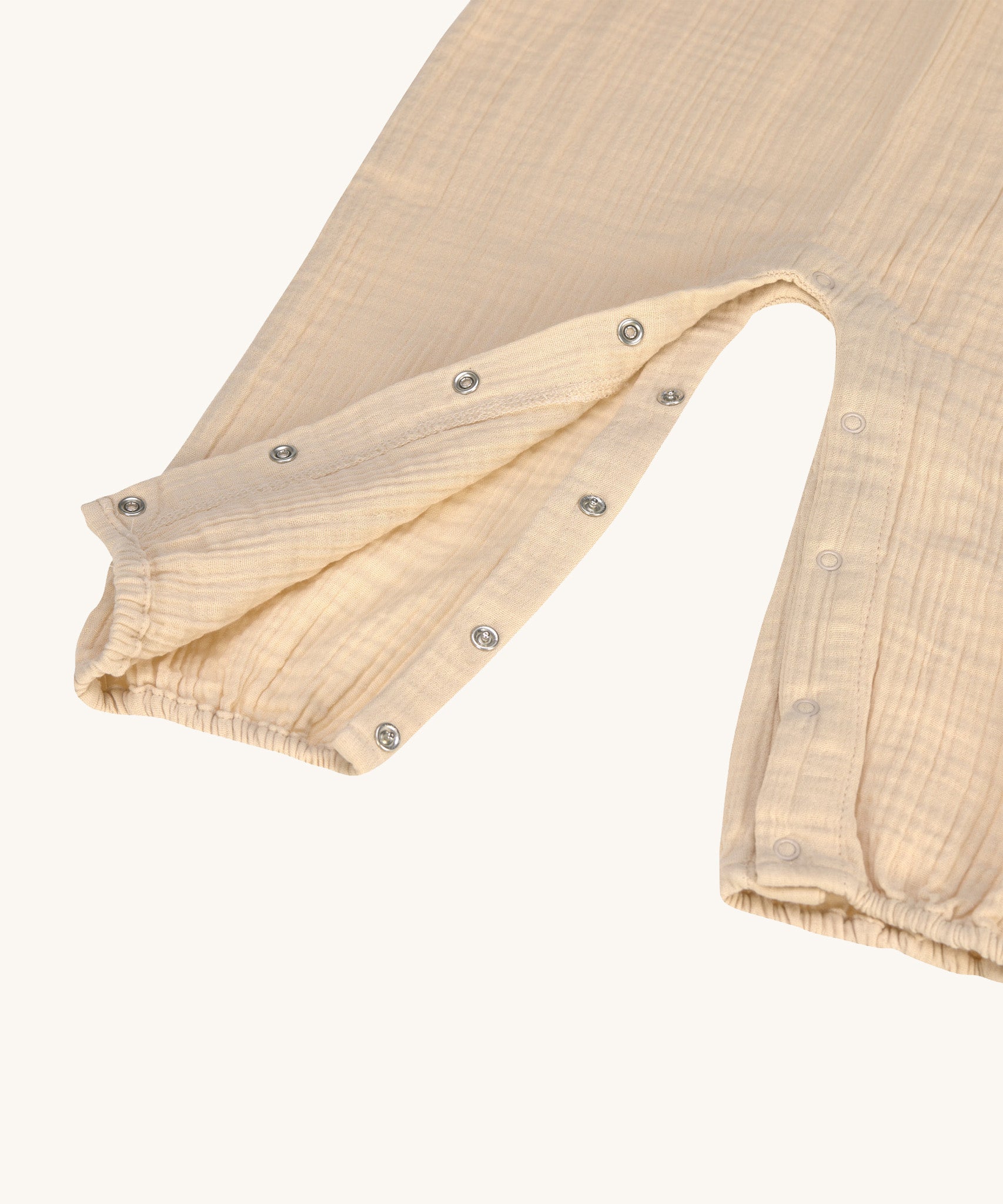 A closeup of the press-in metal fastenings around the leg area of the Lassig organic cotton muslin jumpsuit. 