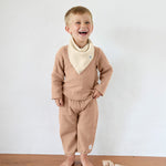 A boy in an organic cotton muslin outfit from Lassig, with the Bandana Dribble Bib in a cream Vanilla colour. 