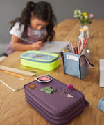 Lassig kids spacy school pencil case in purple on a wooden desk with cute patches and a clip on the elastic loops 