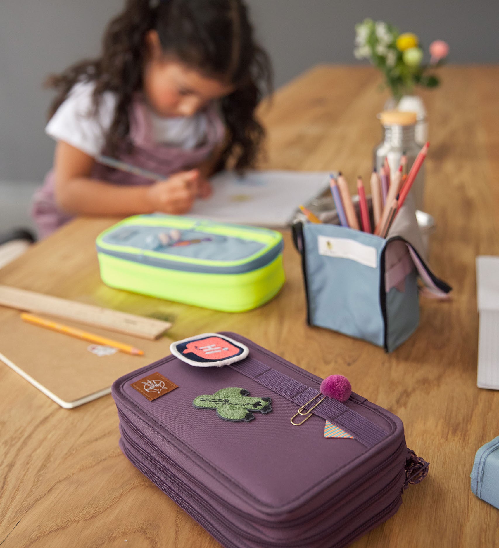 Lassig kids spacy school pencil case in purple on a wooden desk with cute patches and a clip on the elastic loops 