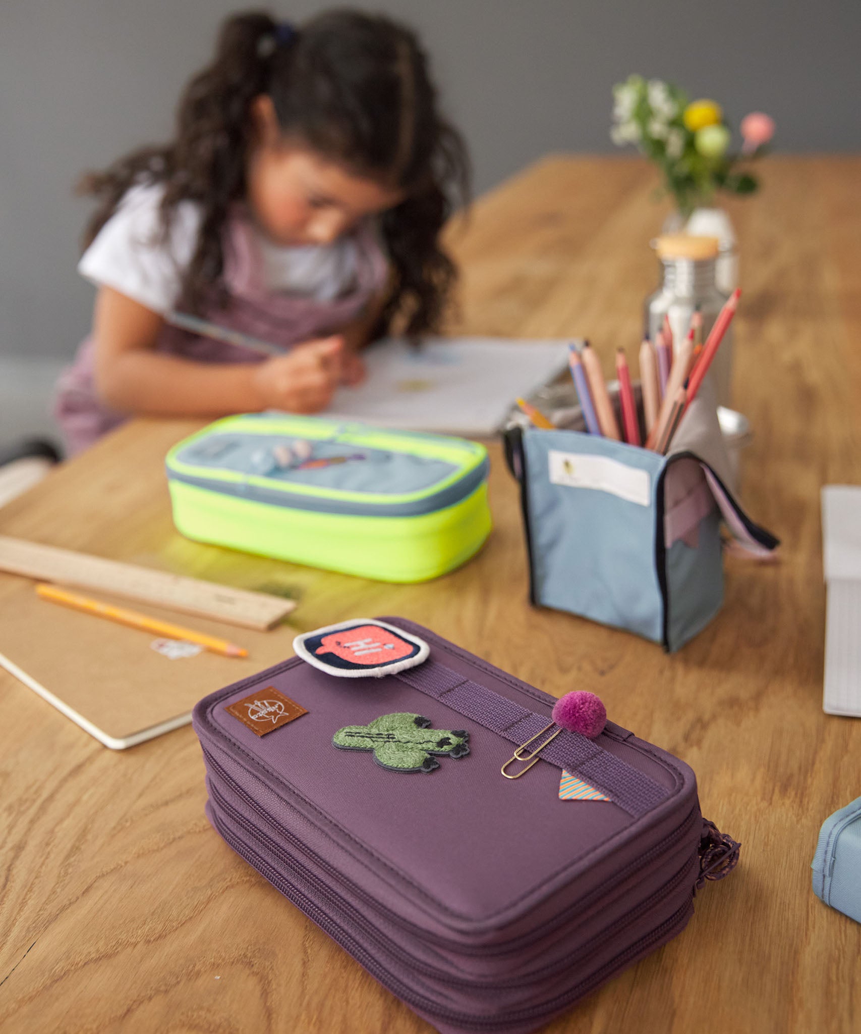 Lassig kids spacy school pencil case in purple on a wooden desk with cute patches and a clip on the elastic loops 