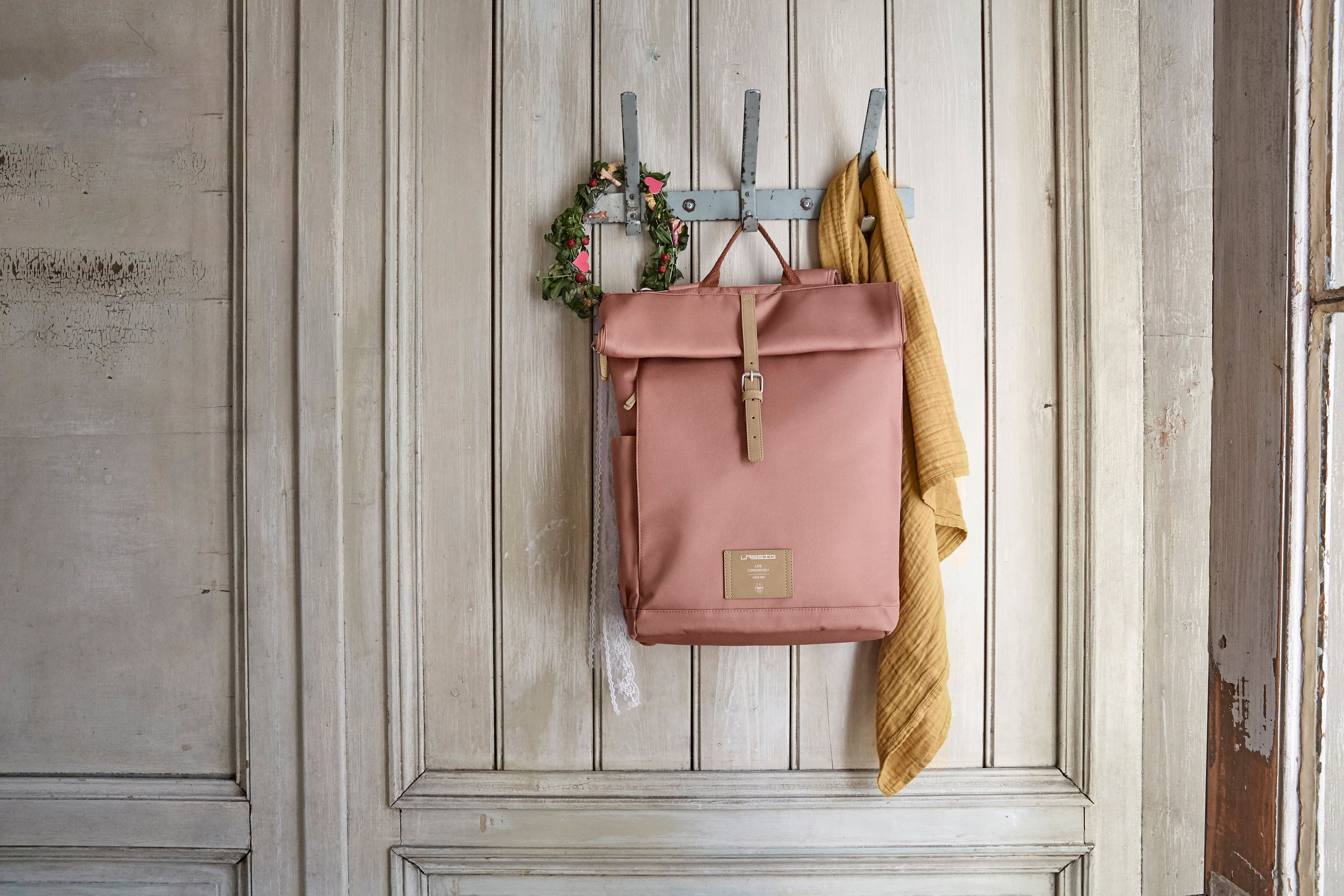 The Lassig rolltop nappy change backpack in cinnamon, hanging on a coat hook