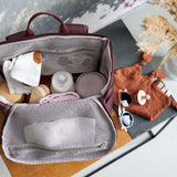 A top view of an opened Lassig Slender Up Nappy change backpack, with a baby bottle, cloths, and more inside.