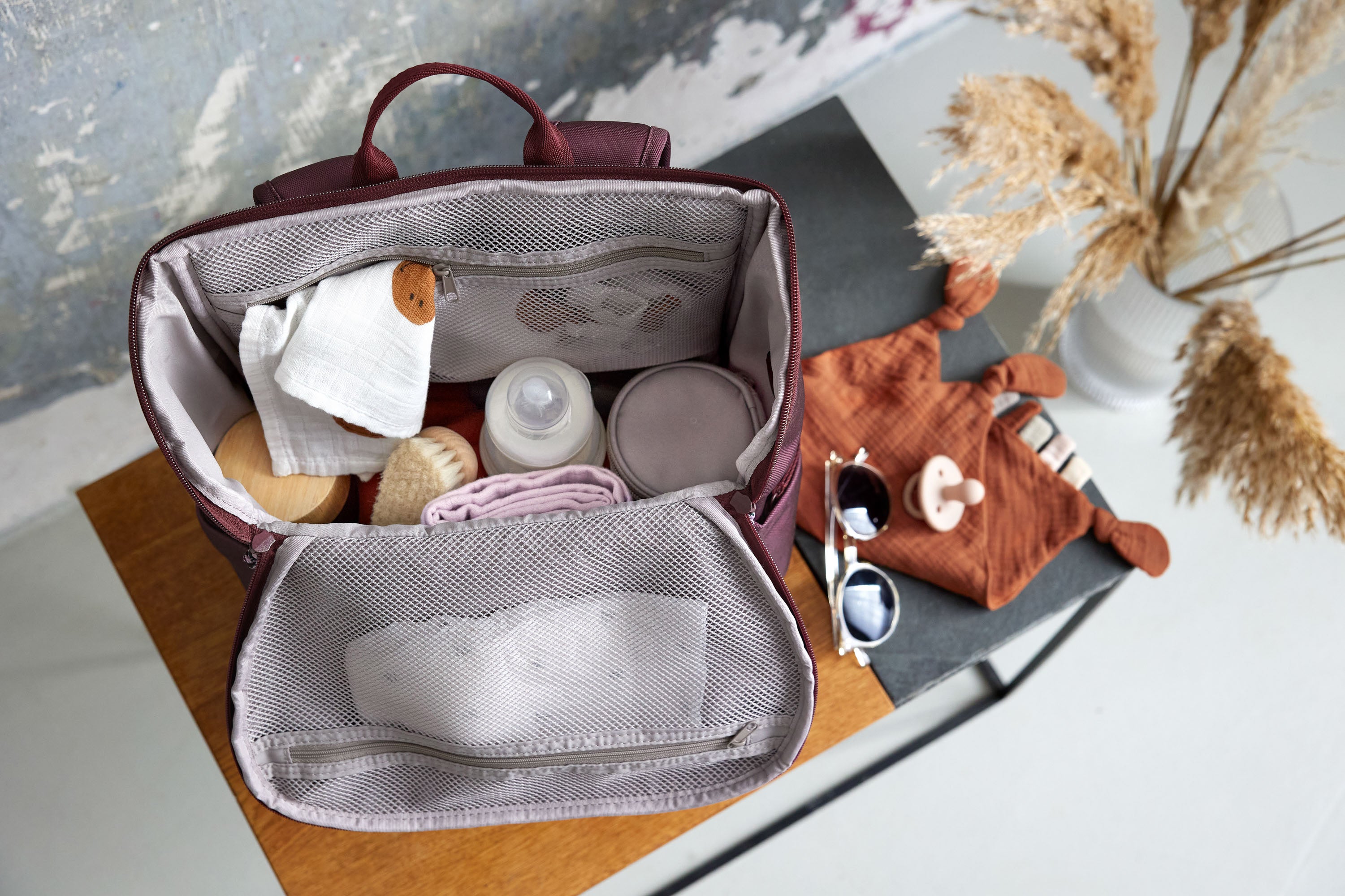 A top view of an opened Lassig Slender Up Nappy change backpack, with a baby bottle, cloths, and more inside.