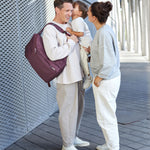A mother and father with their child, the dad is wearing the Lassig Slender Up Nappy change backpack in deep red.