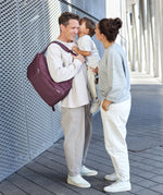 A mother and father with their child, the dad is wearing the Lassig Slender Up Nappy change backpack in deep red.