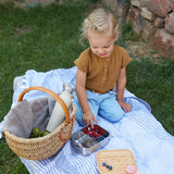 A child sitting outdoors eating berries from a Lassig Stainless Steel Bamboo Lunchbox. This stainless steel lunchbox is part of a wide range of reusable food containers available at Babipur. 