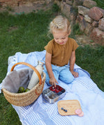 A child sitting outdoors eating berries from a Lassig Stainless Steel Bamboo Lunchbox. This stainless steel lunchbox is part of a wide range of reusable food containers available at Babipur. 