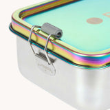 A close up of the clamp latch closure on the Lassig Stainless Steel Lunchbox in a  Solid Bold Rainbow design. A stainless steel lunchbox with removable divider featuring an iridescent rainbow coloured lid. This lunchbox is part of a wide range of reusable items available at Babipur. 