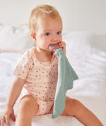 A baby chewing the Lassig rubber strawberry teether, attached to the organic cotton muslin baby comforter.